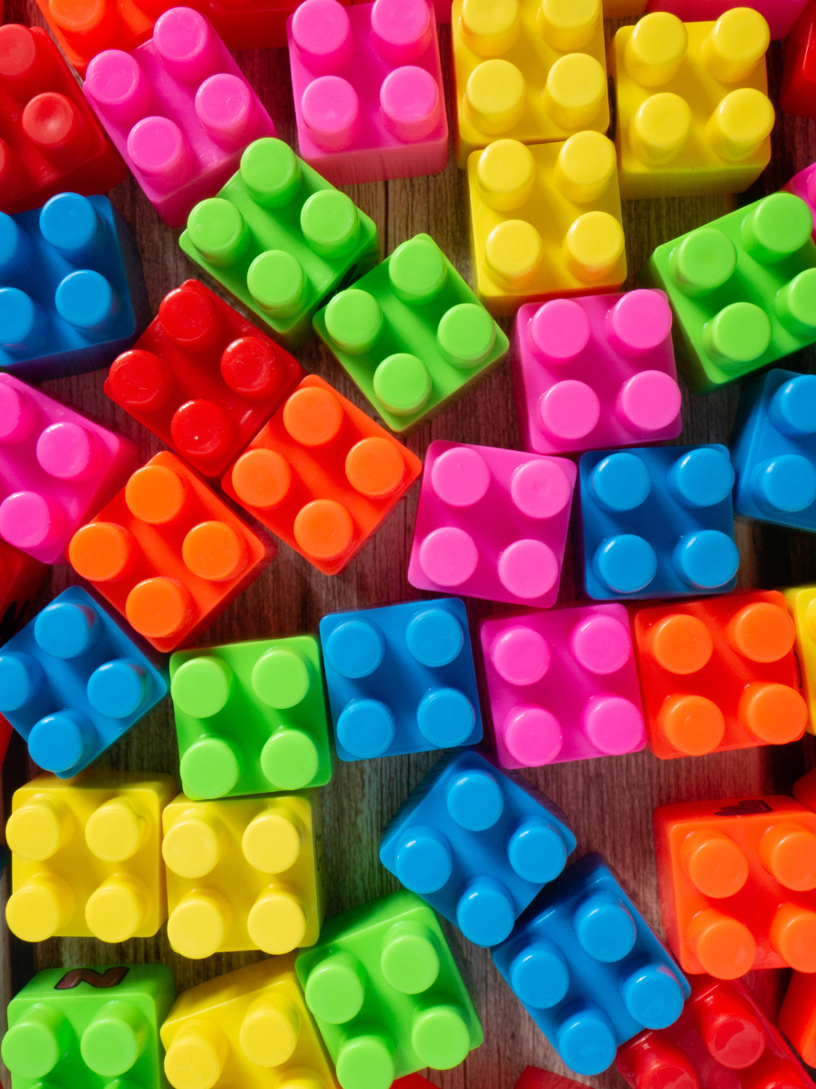 Rainbow-colored, vivid LEGO blocks are scattered against a woodgrain background.