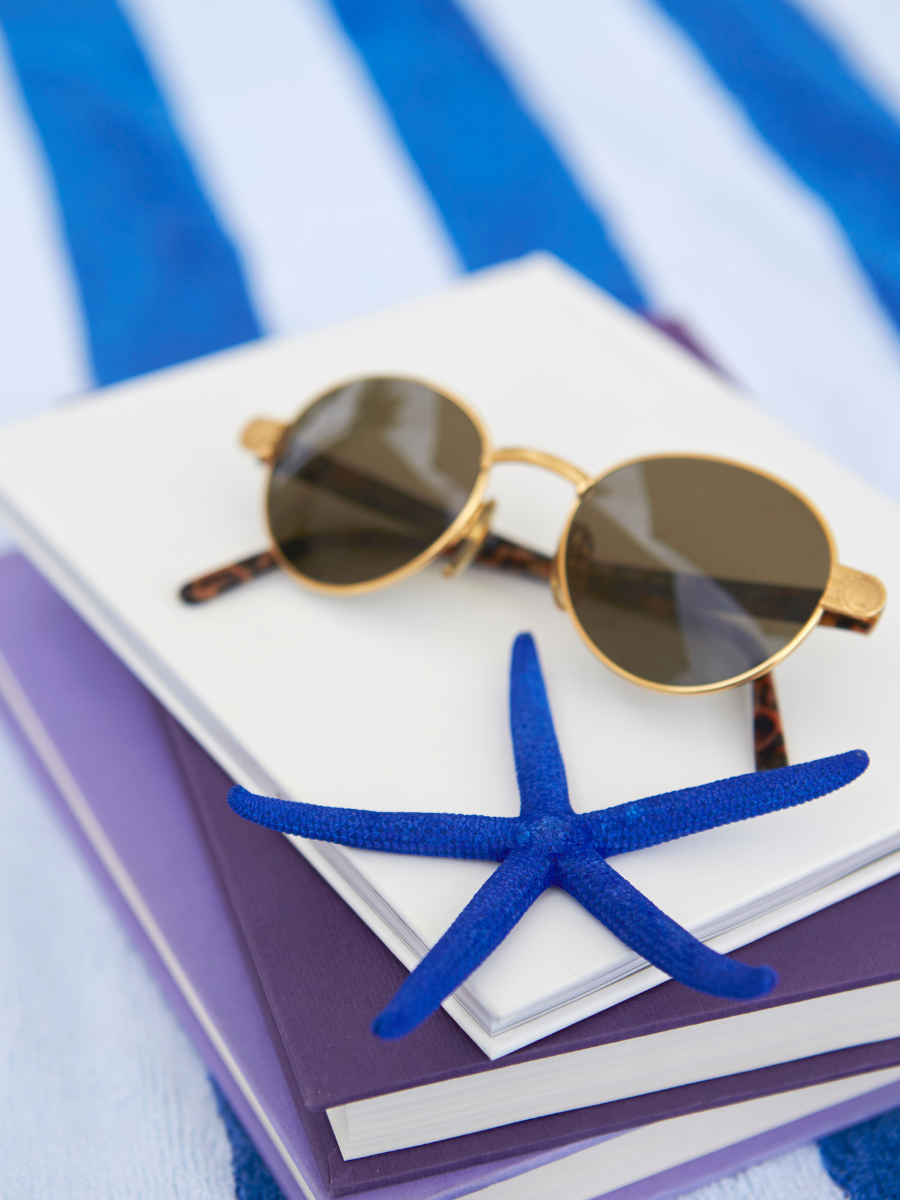 Stack of books on blue and white striped towel with sunglasses and blue starfish