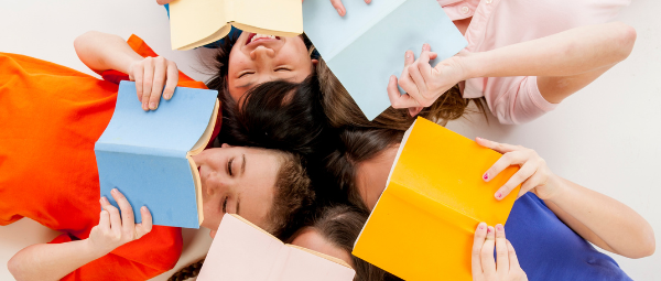 5 children laying on their backs in a circle with their heads together. All of them are holding brightly colored books in front of their faces