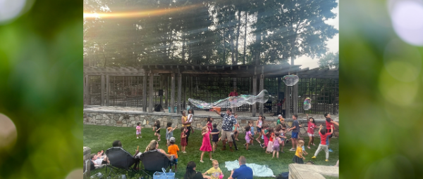 Families dance and run through giant bubbles in an outdoor garden space.