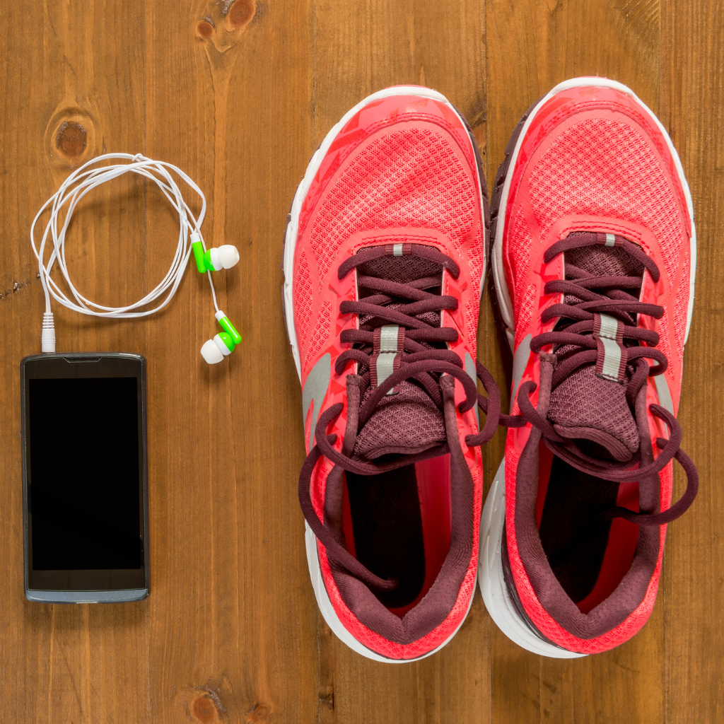 A pair shoes next to a smartphone with wired headphones on a wood floor