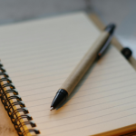 a pen resting atop a blank page in a spiral notebook