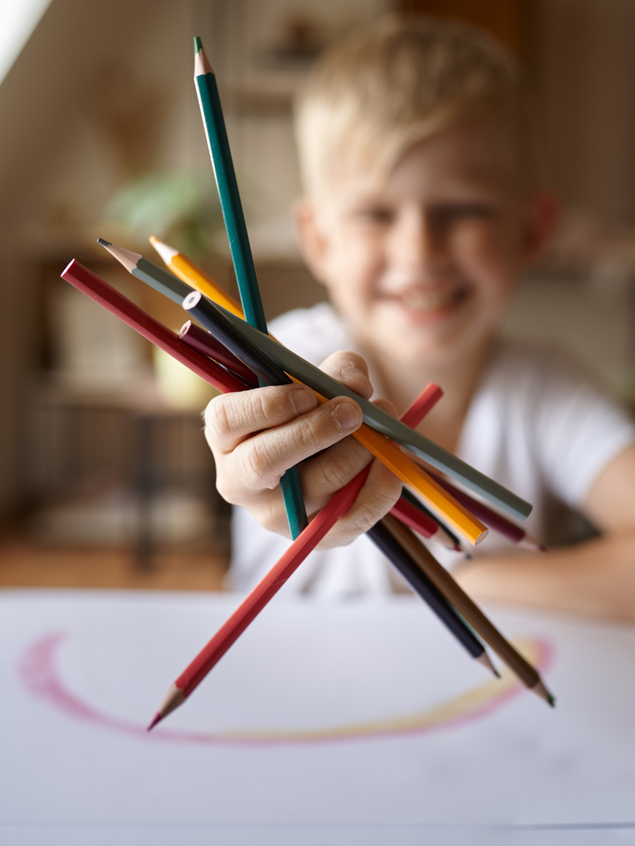 blonde child holding a fistful of different colored pencils