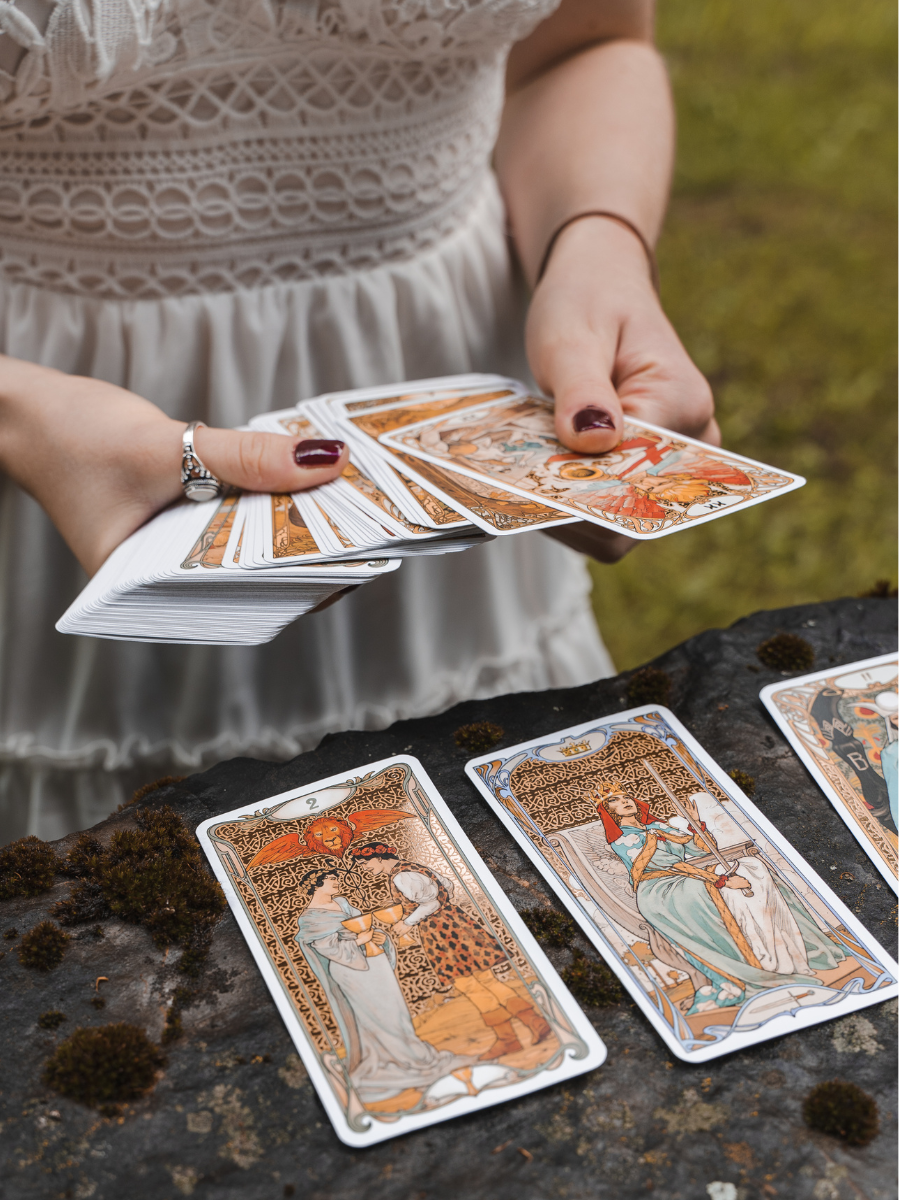 person in white dress holding several tarot cards while standing outside