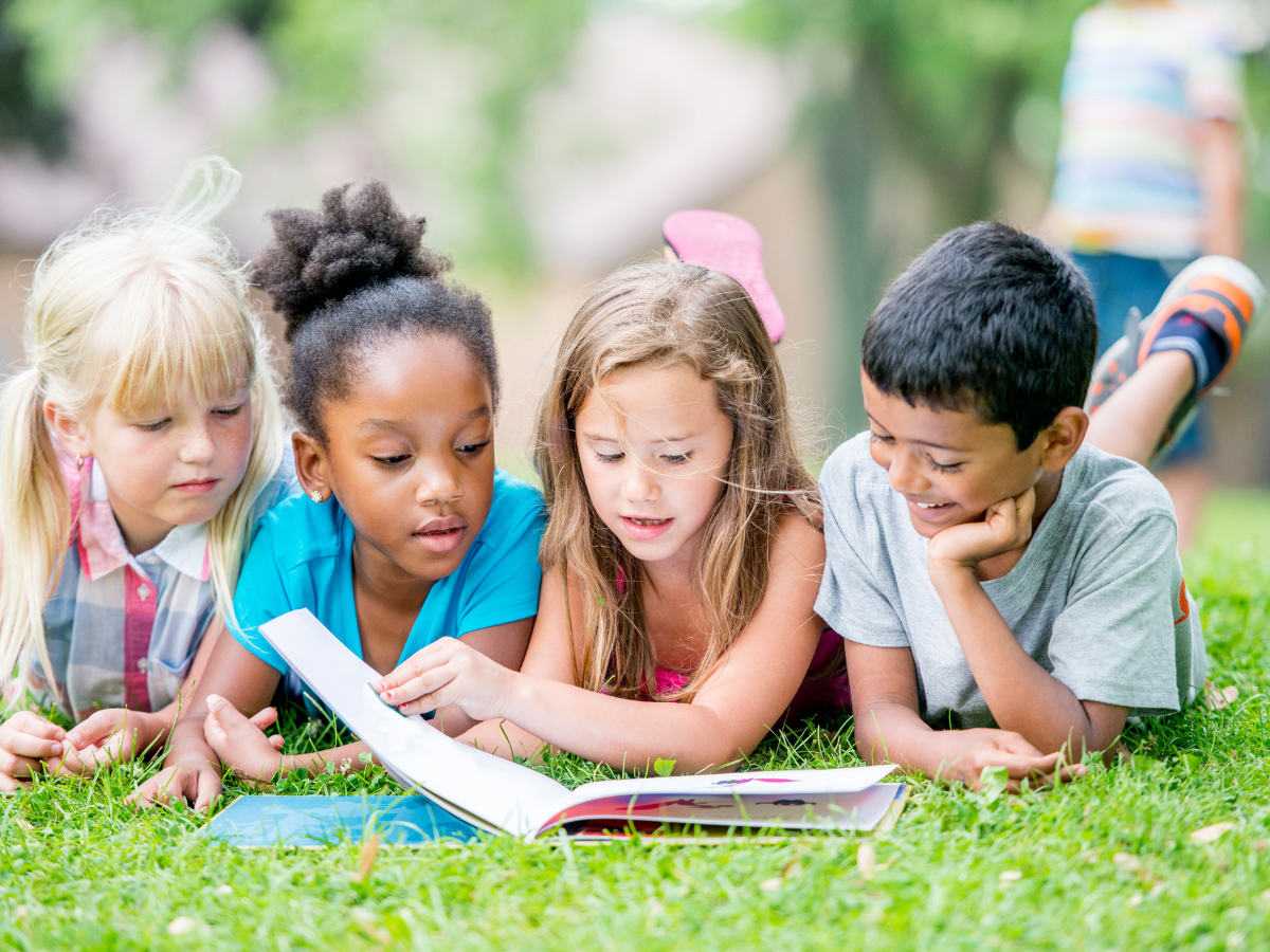 4 children reading one book while laying on grass