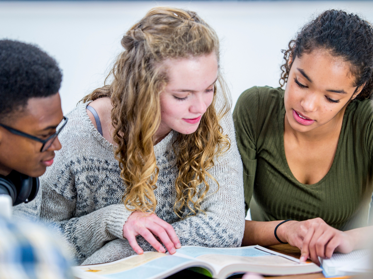 Three teenagers looking at a text book together.