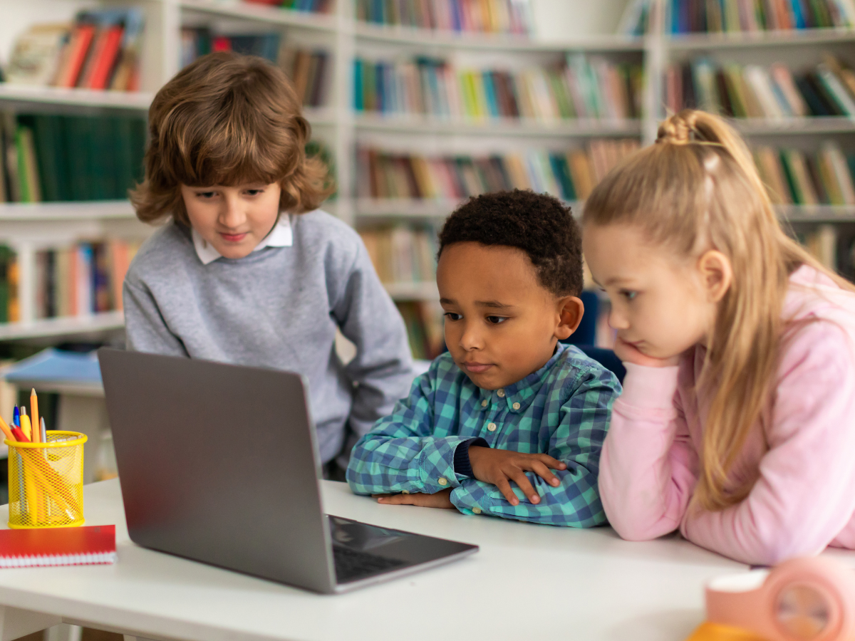 Three children sitting around a laptop in a library