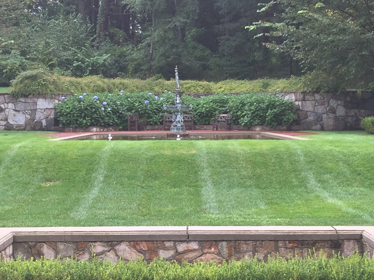 Queset Garden in summer with green lawn, fountains, and green bushes in background